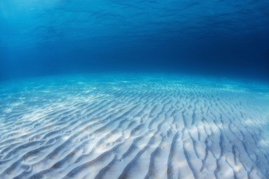 underwater shoot of an infinite sandy sea bottom with clear blue water and waves on its surface