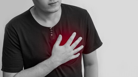 people, health care and problem concept-a young man suffering from heart pain on a gray background holding on to the heart