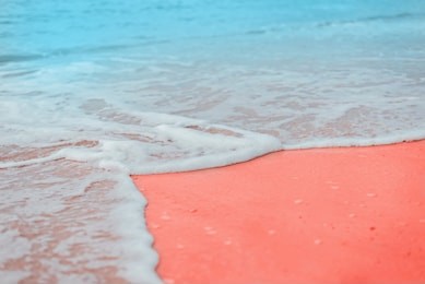 soft blue waves of the sea with white foam on sandy beach toned living coral creative and moody color of the picture.