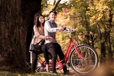 happy couple riding on retro bicycle against the autumn background trees. the man runs a bicycle, a girl sits behind. romantic image of two people on vacation. honeymoon image of young people.