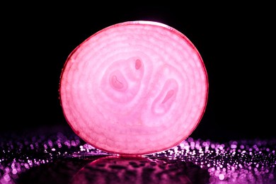 slice of raw onion with water drops and neon pink back light on black background