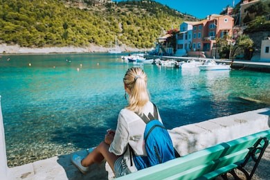 woman tourist sitting on the bank in front of beautiful sea bay on summer morning. lovely vacation in assos village with beautiful traditional houses and pine groove. kefalonia, greece
