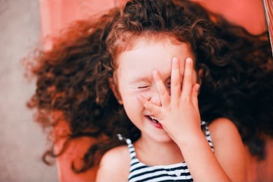 portrait of smiling curly funny girl outside. authentic toddler in the city inspired by living coral - color of the year 2019