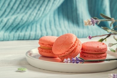 close up, macro. provence breakfast. color living coral. sweet french macarons on a round plate, a vintage buttons, a lavender. turquoise knitted background. copy space.