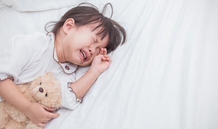 portrait of little asian crying girl with little rolling tears weeping emotion, closeup young girl hurt in pain crying in white bed with copy space. lonely depress stress angry unhappy concept