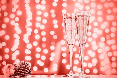 two glasses of champagne with christmas toys. festive lights bokeh christmas background. new year holidays celebration. horizontal, toned, delicate lilac. living coral theme - color of the year 2019