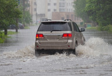 red car rides in heavy rain on a flooded road