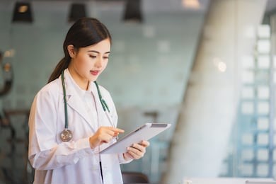 female asian doctor using a digital tablet & wearing a white coat.