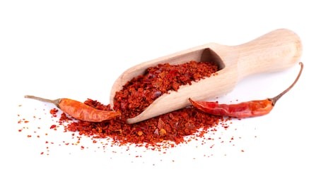 dry and crushed chili pepper flakes isolated on white background. red chili peppers in a wooden spoon.