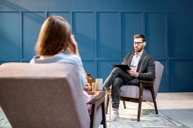 handsome male psychologist listening to the woman client sitting during psychological session in the blue office interior