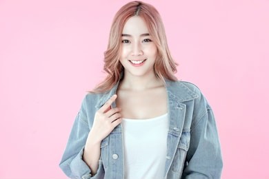 asian woman smiling with blue jean clothing, pink background
