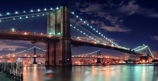 brooklyn bridge over east river at night in new york city manhattan with lights and reflections.