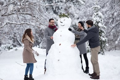 two young couples having fun by building big snowman in park during winter holidays