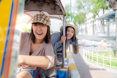 beautiful chinese or japanese woman drive auto rickshaw and her thai friend is sitting behind her. they are closed friend and always travel together. they’re going to touristic place with happy faces