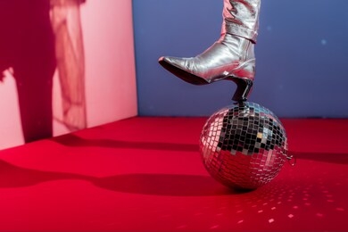cropped view of model in metallic footwear posing with disco ball on pink and blue background