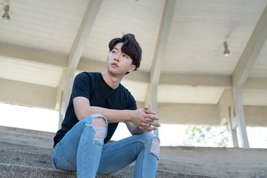 handsome asian casual man sit on a staircase posing on grandstand background.
portrait of young korean against staircase background.