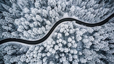 curvy windy road in snow covered forest, top down aerial view.