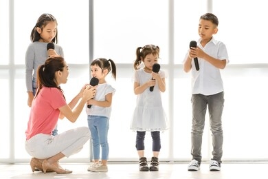 asian teacher teach asian kids to sing a song, kids pay attention to listen to her, they stand in front of big white window. concept for music school or singing classroom training.