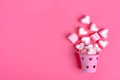 marshmallows and heart shaped candies spilled from a pink iron bucketon a pink background happy valentine's day flat lay top view