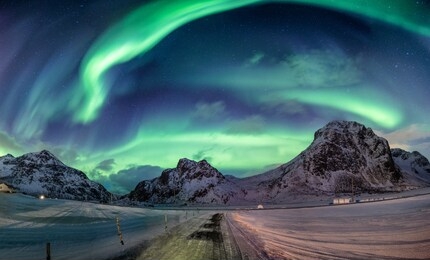 northern lights explosion on snowy mountain range near coastline at lofoten islands, norway