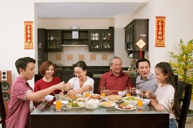 parent, grandparents and children enjoying good food at lunar new year celebration, couplets with best wishes for coming year in the background