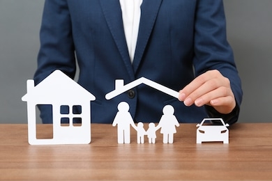 woman with cutout paper family, house and car at table, closeup. life insurance concept