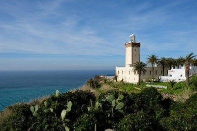 famous tangier white lighthouse near blue ocean and blue sunshine sky in morocco. green cactus as foreground . cape malabata with a lighthouse.promontory at the entrance to the strait of gibraltar. 