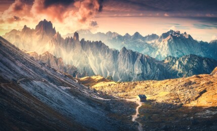 small house in beautiful mountain valley, dramatic sky with red clouds and yellow sunlight at sunset. autumn landscape with mountains in tre cime park in dolomites, italy. italian alps in fall