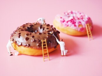close up miniature painting color on donut over pink background.