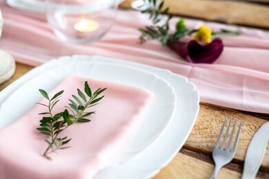 rustic table setting: pink napkin folded on a plate, tableware, candle, flowers