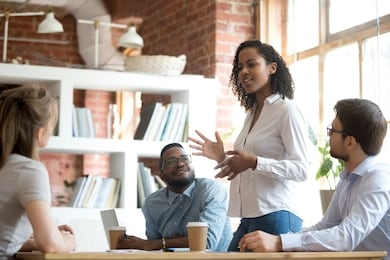 ambitious smart african black female employee speaking at diverse meeting share creative idea opinion at group briefing while jealous envious skeptical male coworkers looking listening to colleague