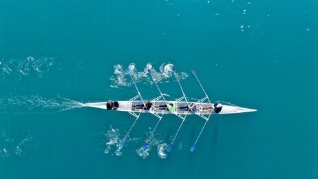 aerial drone bird's eye view of sport canoe operated by team of young women in turquoise clear waters