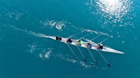aerial drone bird's eye view of sport canoe operated by team of young women in emerald clear sea
