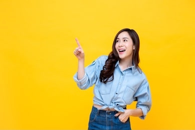 beautiful smiling asian woman pointing hand to empty space aside studio shot isolated on colorful yellow background