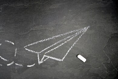 with a chalk drawn a paper plane and a dashed way on a dark marble surface - background with a flying paper plane