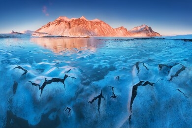 cracks on the surface of the blue ice. frozen lake in winter mountains. blue sky with sun light and high mountains on background. beautiful winter panorama. 