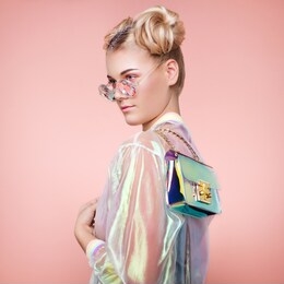 blonde young woman in holographic jacket. lady in stylish pink eyeglasses. model with holographic foil handbags. beauty fashion make-up