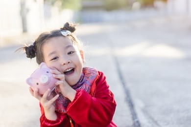 4 years old asian chinese child girl.happy little asian girl in chinese traditional dress smiling and holding holding pink piggy bank.happy chinese new year concept. 