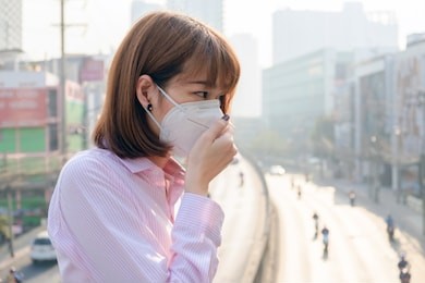 asian woman wearing the n95 respiratory protection mask against air pollution at road and traffic in bangkok, healthcare concept 
