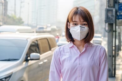 asian woman wearing the n95 respiratory protection mask against air pollution at road and traffic in bangkok, healthcare concept 