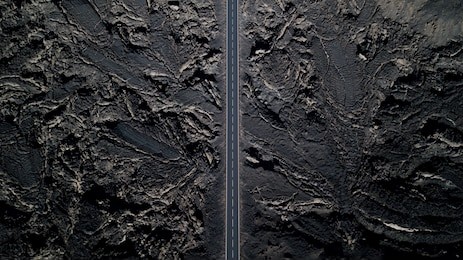 the road with white lines is surrounded by black volcanic lava. sticking rocks. dangerous adventure of incredible beauty. top view, drone footage. minimalistic landscape.