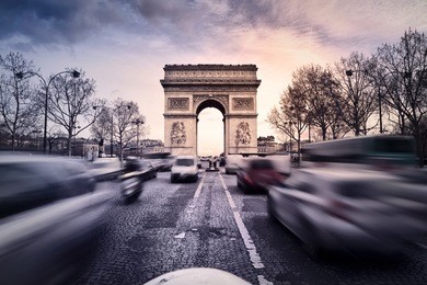 arc-de-triomphe on the champs-elysees in paris, france, at sunset. heavy traffic on the avenue.