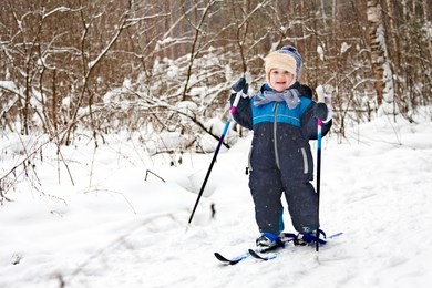 happy toddler is skiing in winter forest