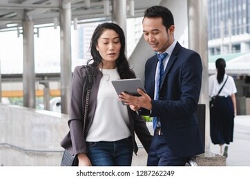 happy asian businessmen discussing with female boss in the city. male open application in tablet showing data to present work.