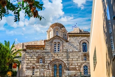 an ancient greek church in the plaka district of athens greece with the ancient acropolis hill behind as tourists enjoy the views underneath the flag of greece.