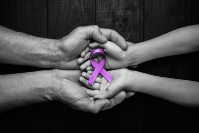 hands holding purple ribbons top view on black wooden background. alzheimer's disease, epilepsy, fibromyalgia awareness, world cancer day. black and white. symbol of fighting child abuse.