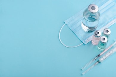 medical bottle, vials, syringes and face mask on blue background with copy space. vaccination session and immunity improvement.
