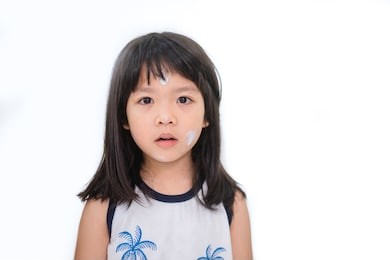 close up of little asian girl putting sun screen cream on her face isolated on white background.summer vacation and protection face skin from sun.