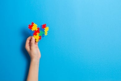 child hand holding colorful heart on blue background. world autism awareness day concept