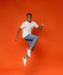 funny portrait on young african-american man in humorous jump on orange background
